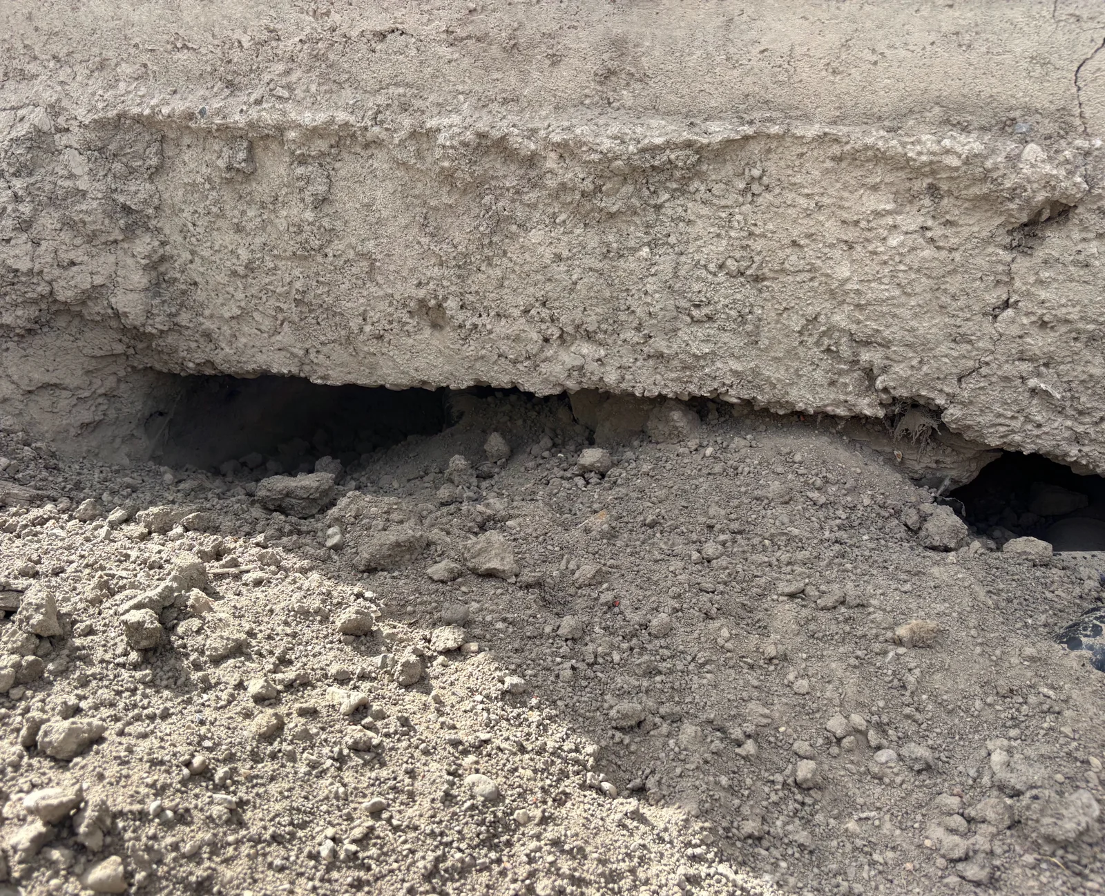 Visible gap beneath a concrete slab where supporting soil has washed away