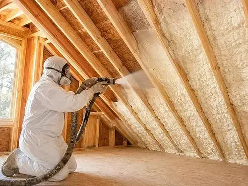 Installer spraying insulation along timber roof framing